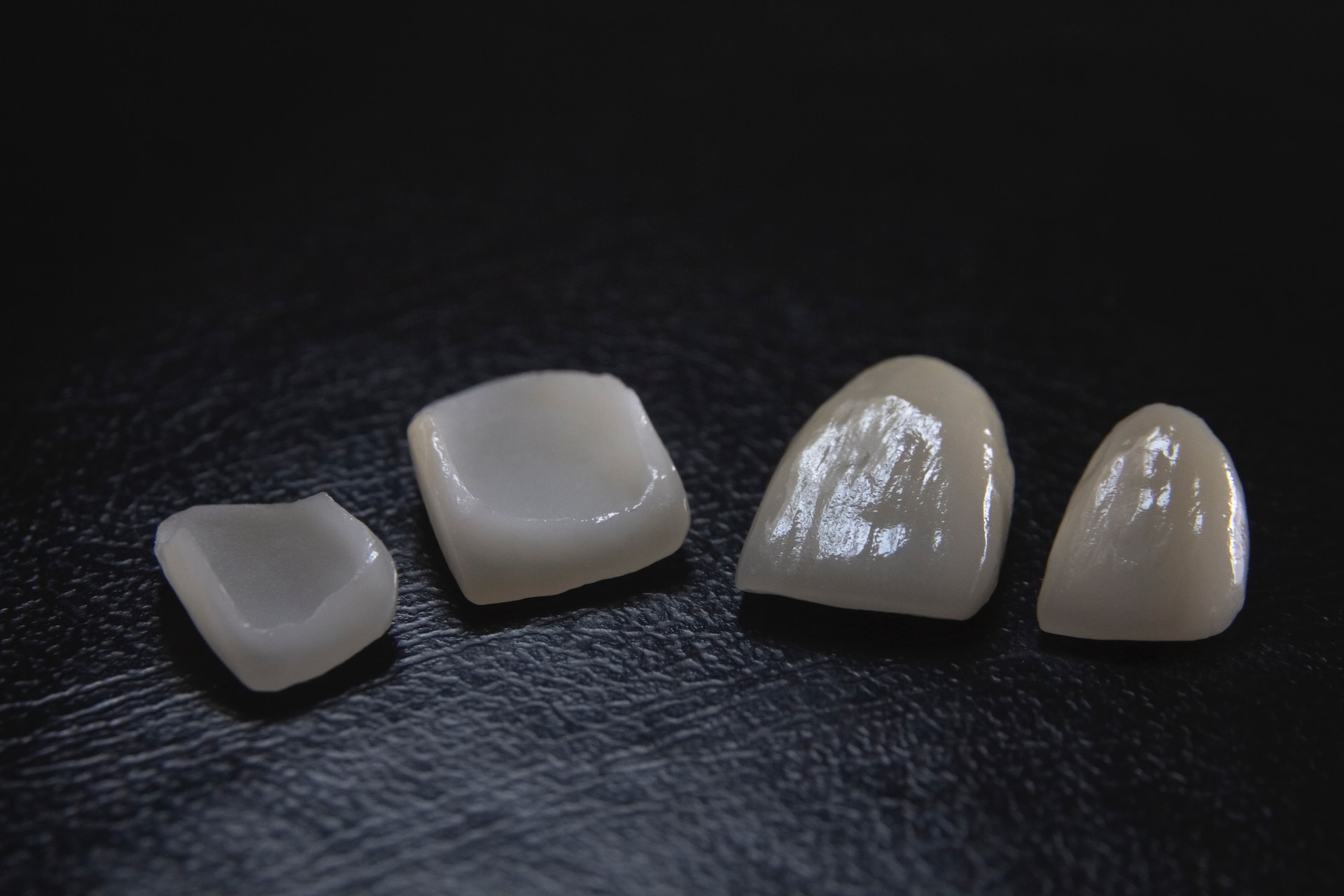 four porcelain dental veneers on grey surface