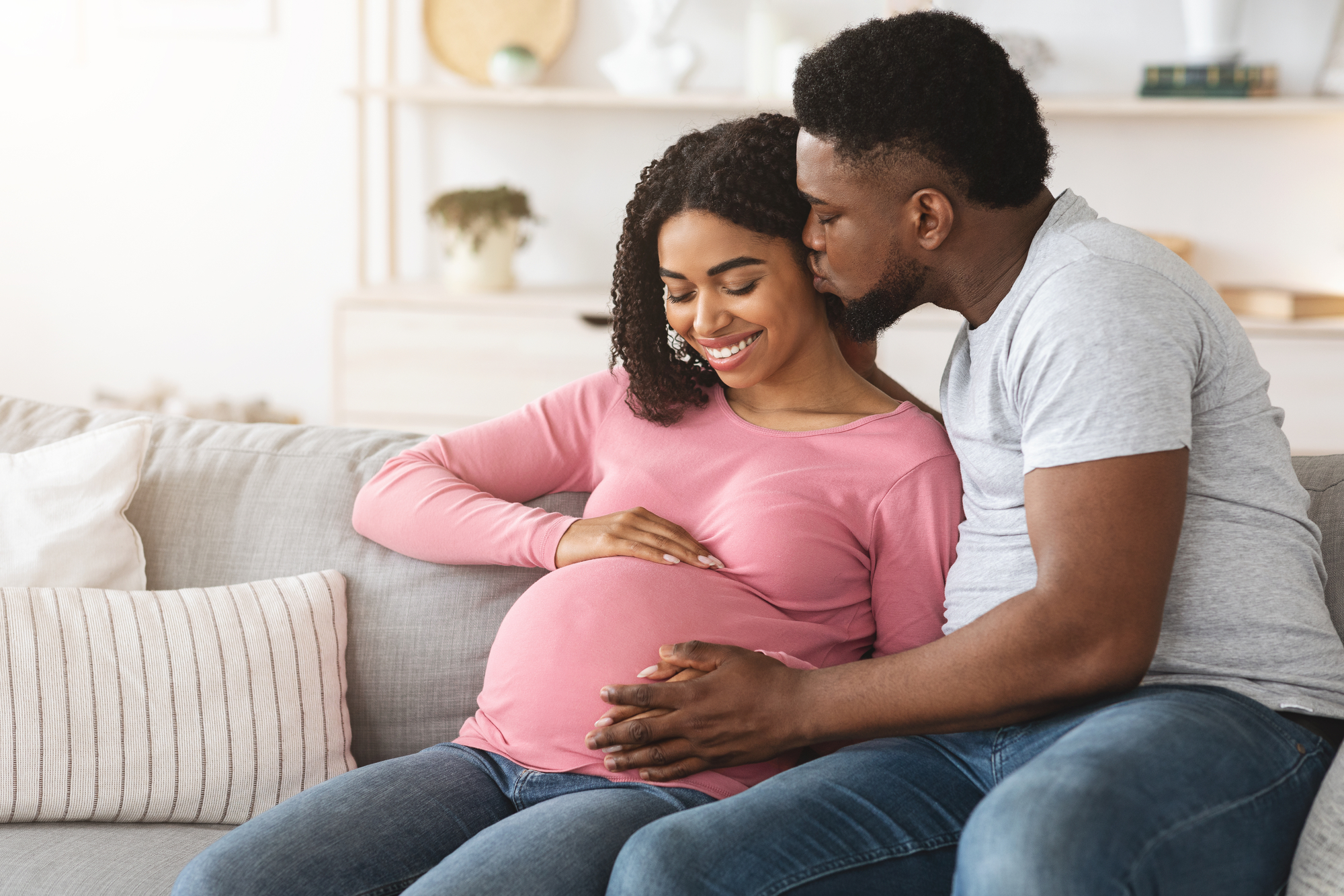 black man kissing his pregnant wife while sitting on the couch